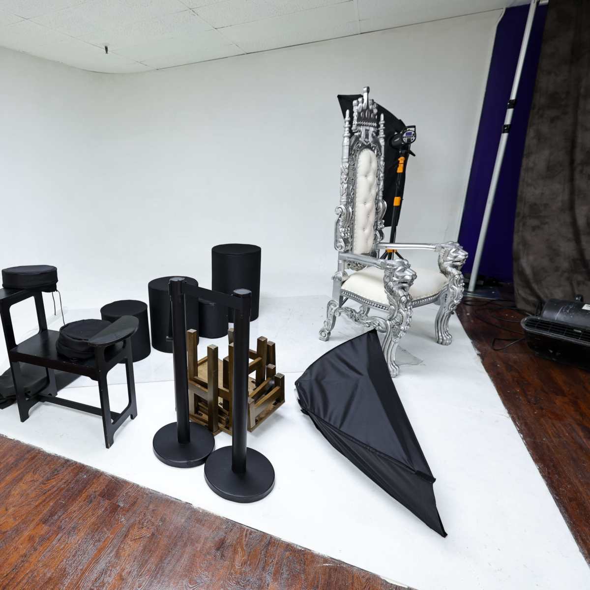 A photography studio setup with various props, including a white backdrop, a throne-like chair, and several stands and black drapery pieces.