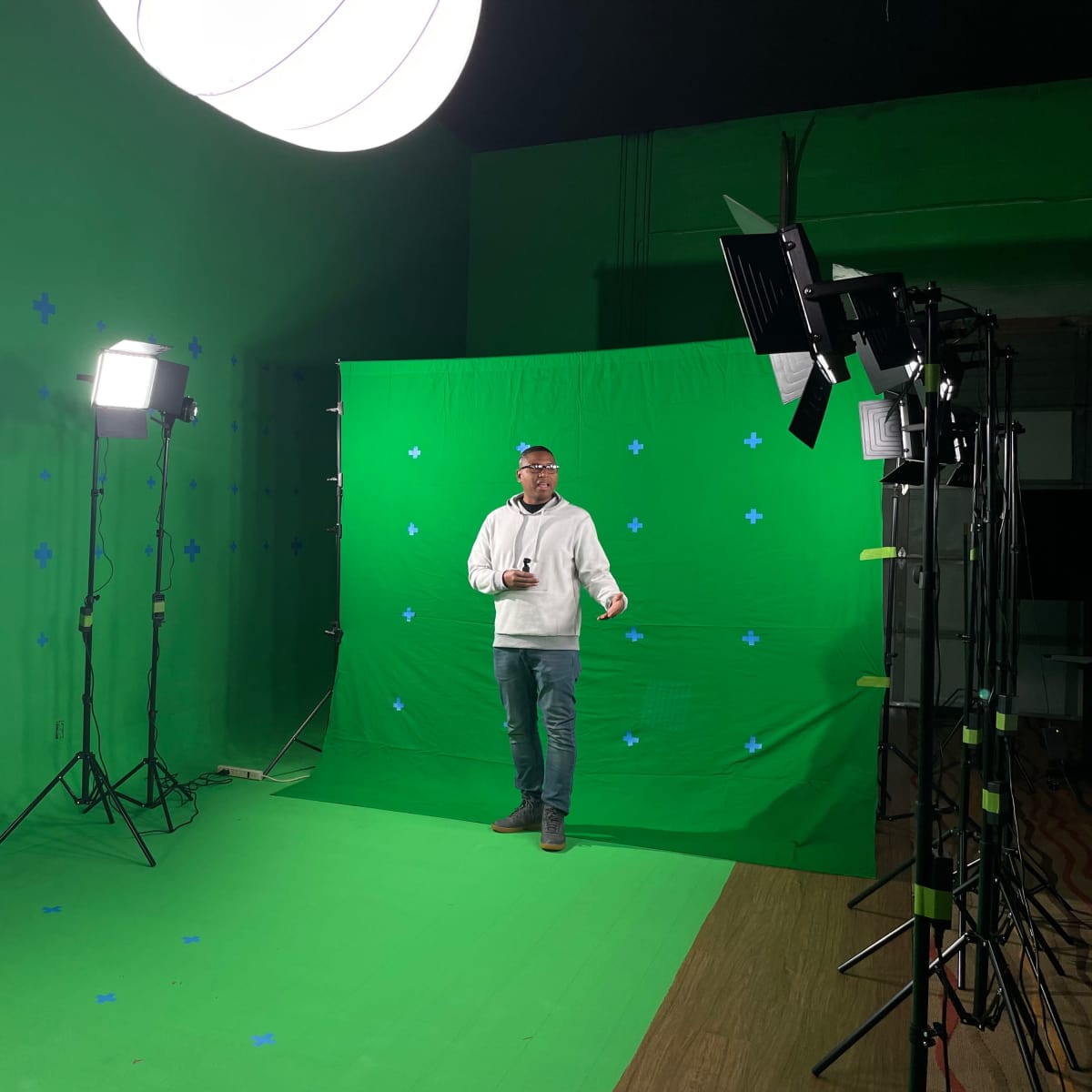 A man stands in front of a green screen setup, surrounded by studio lights and equipment.