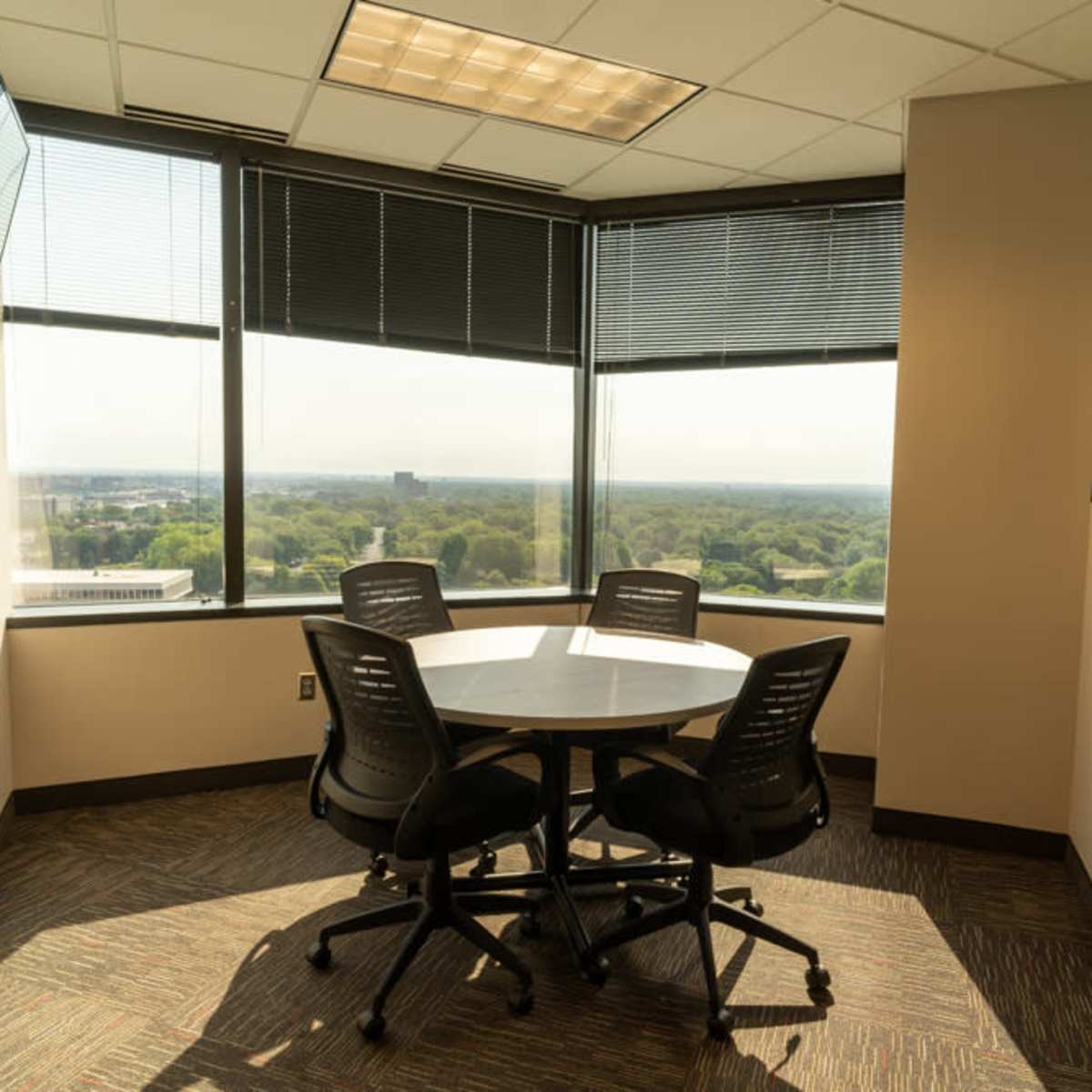A small conference room with a round table and four chairs is situated in a corner, featuring large windows that offer a view of the surrounding landscape.