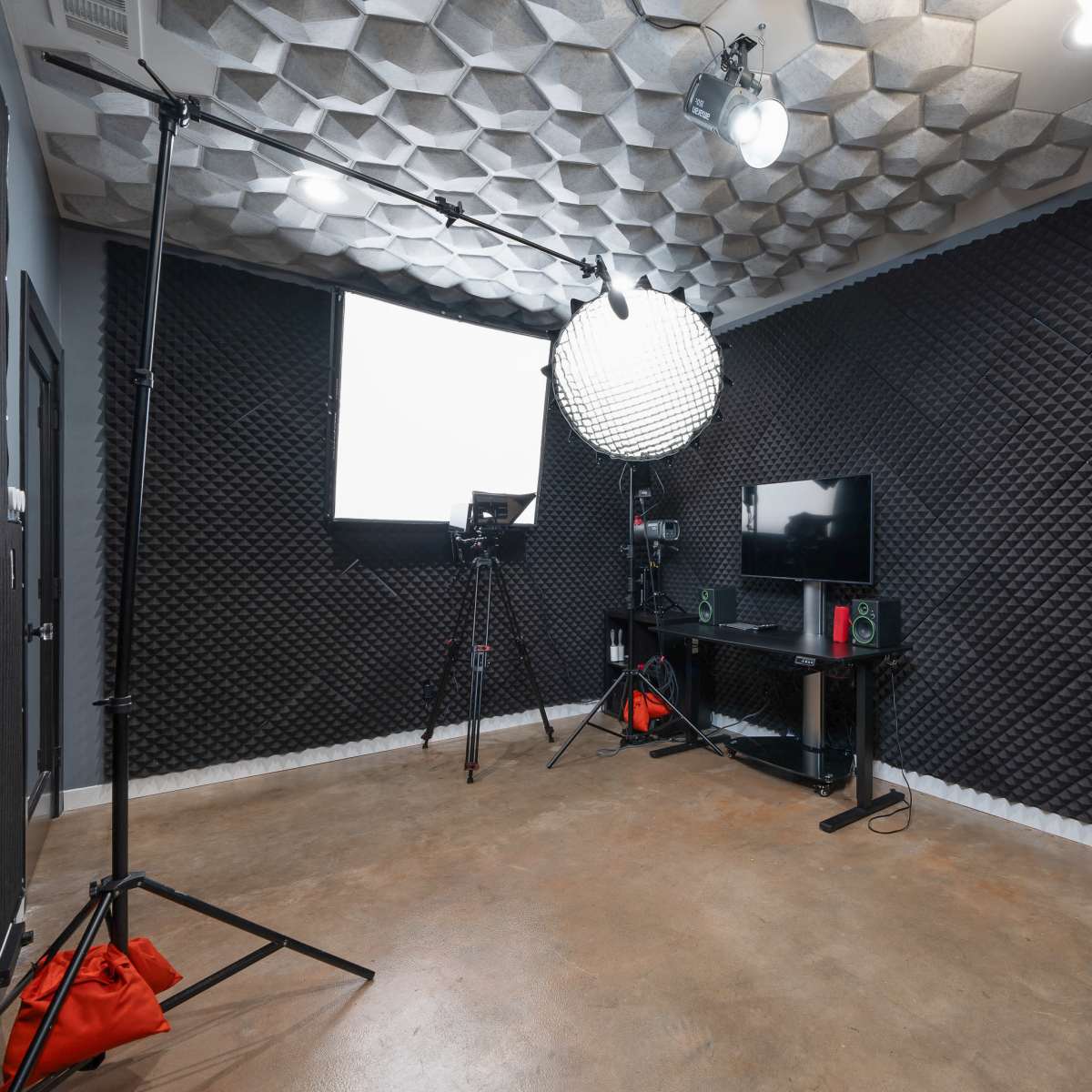 A soundproofed studio equipped with a lighting setup, camera tripod, and audio equipment arranged around a TV on a black shelf.