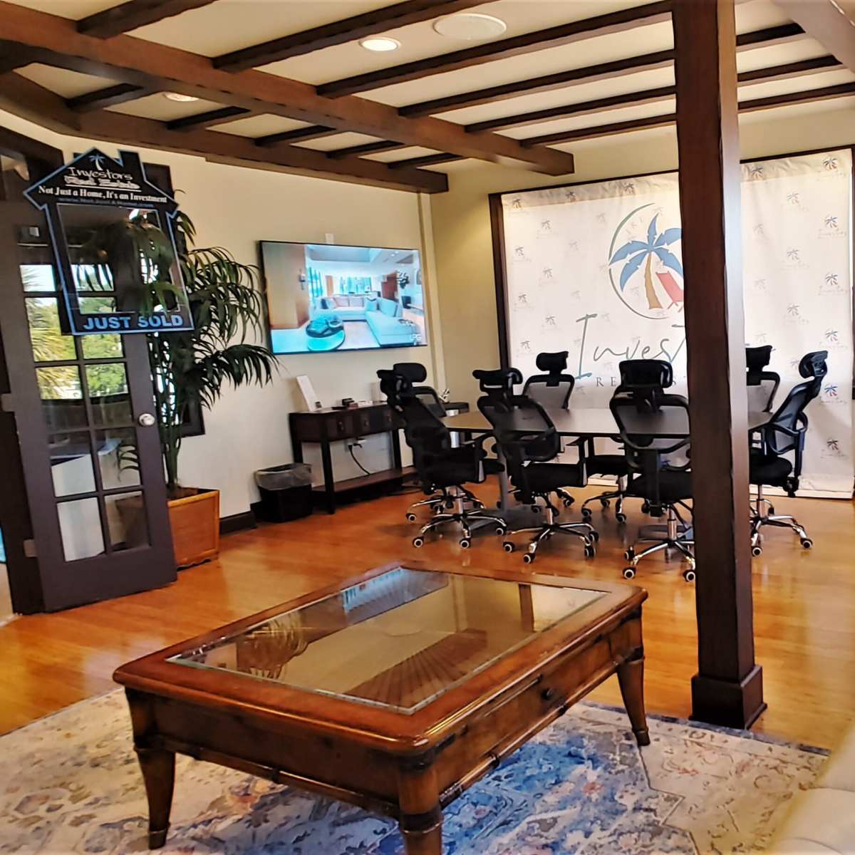 A modern office space featuring a conference room with a large table and ergonomic chairs, a reception area with a television, and large windows letting in natural light.