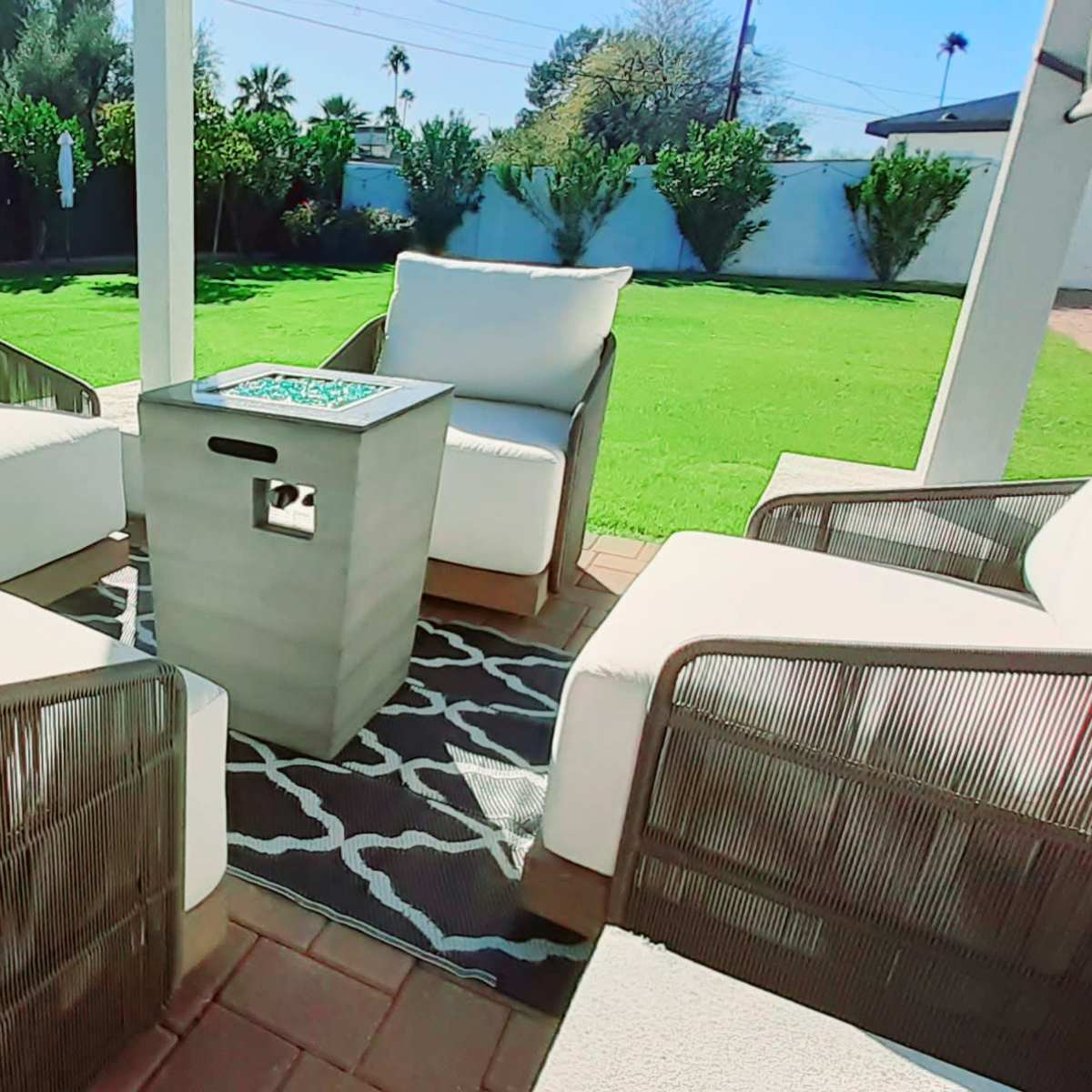 A patio features four cushioned chairs arranged around a small table on a grassy lawn.