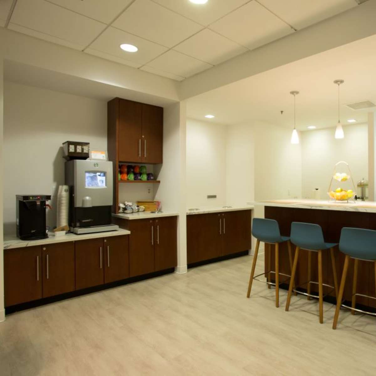 A modern kitchen with a central island, three blue bar stools, coffee maker, stainless steel refrigerator, and seating area.