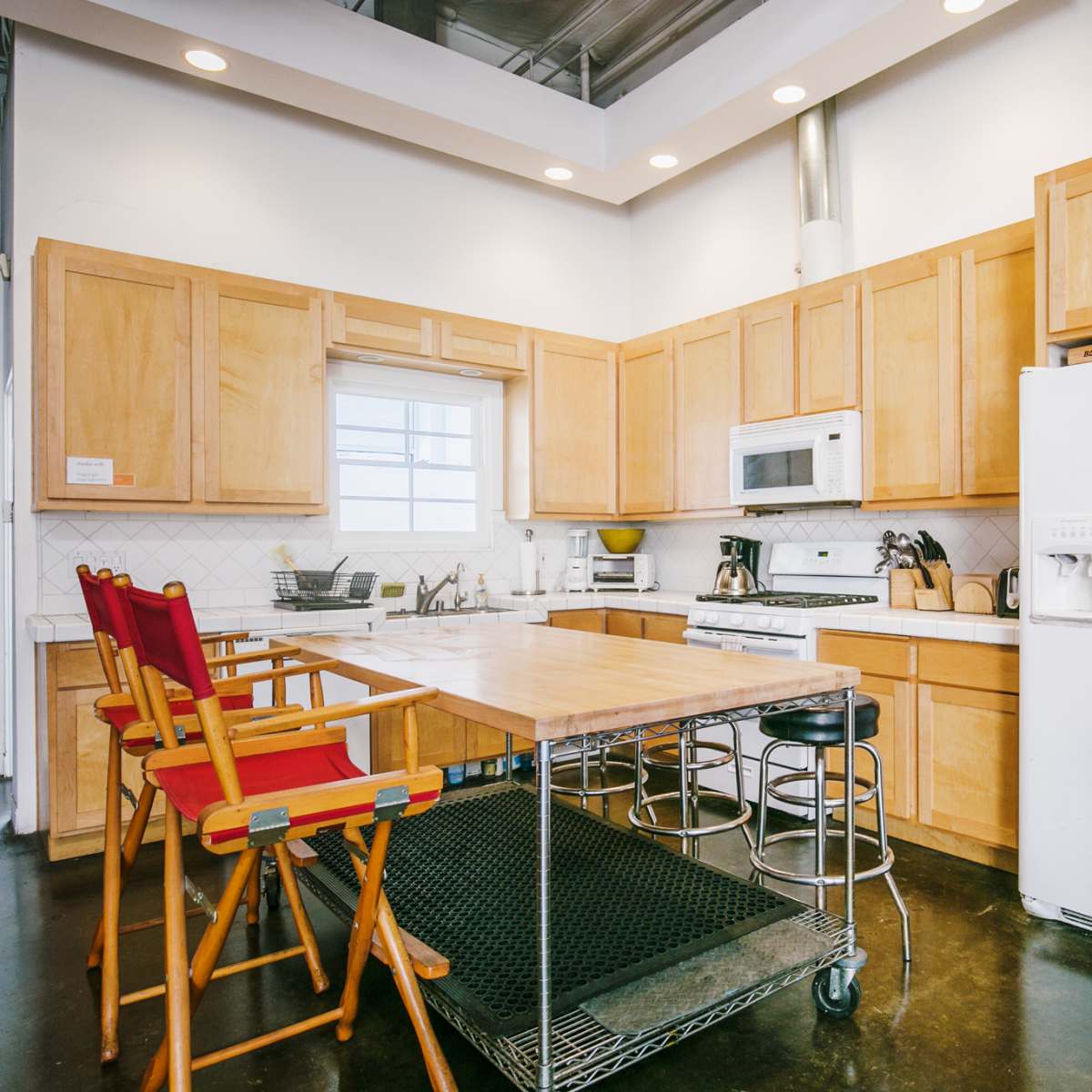 A modern kitchen with wooden cabinetry, a white refrigerator, a stove, and a central island with red and black seating.