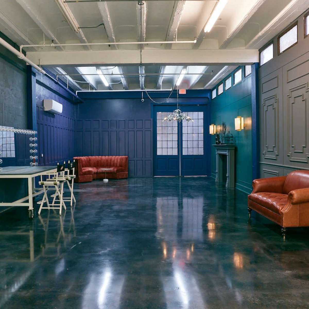 A spacious room with polished concrete floors, blue and gray walls, a large mirror, a vanity table, two leather sofas, and stylish lighting fixtures.