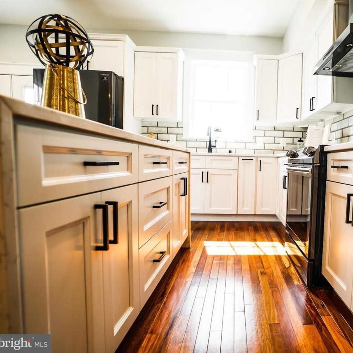 A modern kitchen with white cabinetry, stainless steel appliances, and wooden flooring.