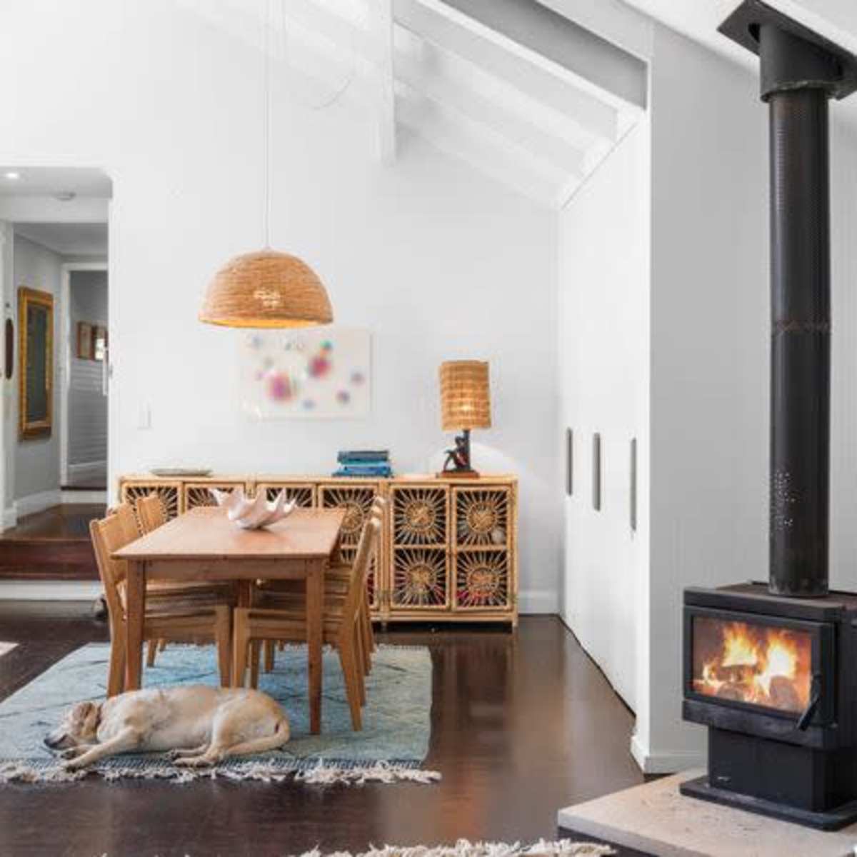 A modern living space with a dining area, a wood-burning stove, and a sleeping dog on a rug.