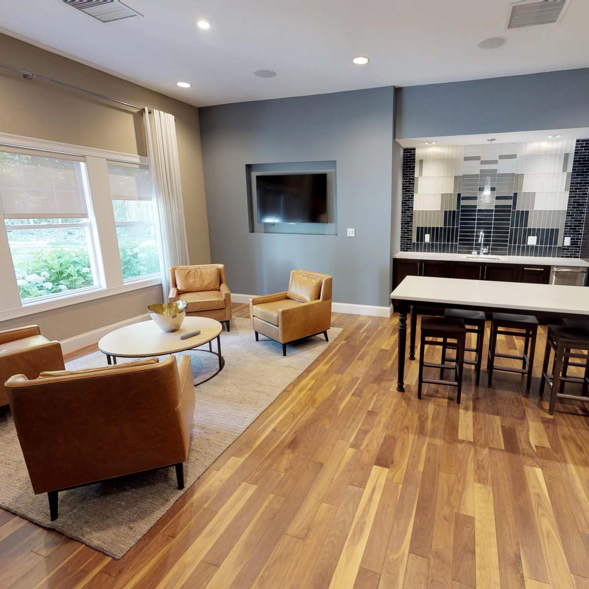 A modern living space with a seating area featuring two armchairs and a coffee table, alongside a kitchen with barstools and sleek appliances.