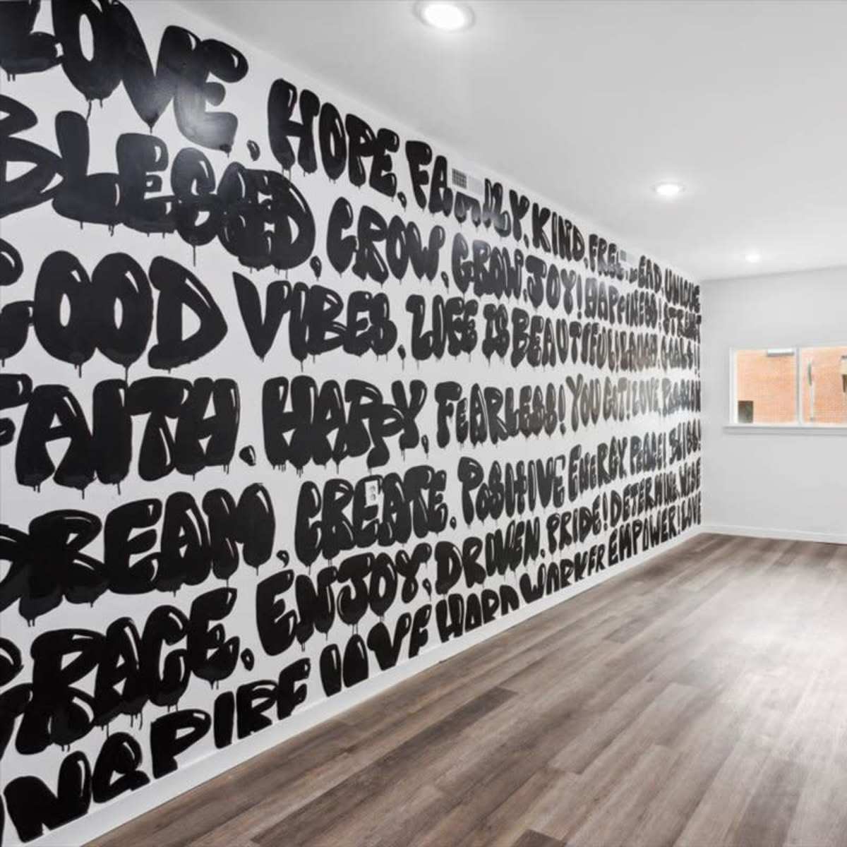A spacious, brightly lit room features a wall covered in large, bold black text with positive affirmations, and a blue front door on the right.