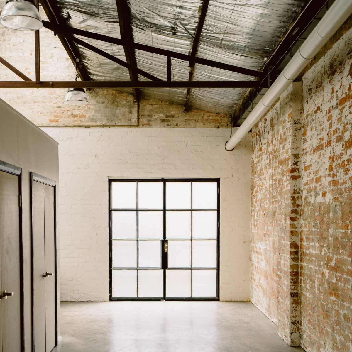 A spacious interior room with exposed brick walls, a concrete floor, and large glass doors leading to the outside.