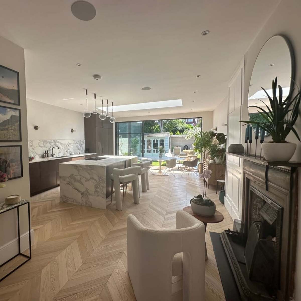 A modern, open-concept kitchen and living area with marble countertops, a large window leading to an outdoor space, and several decorative photographs on the walls.