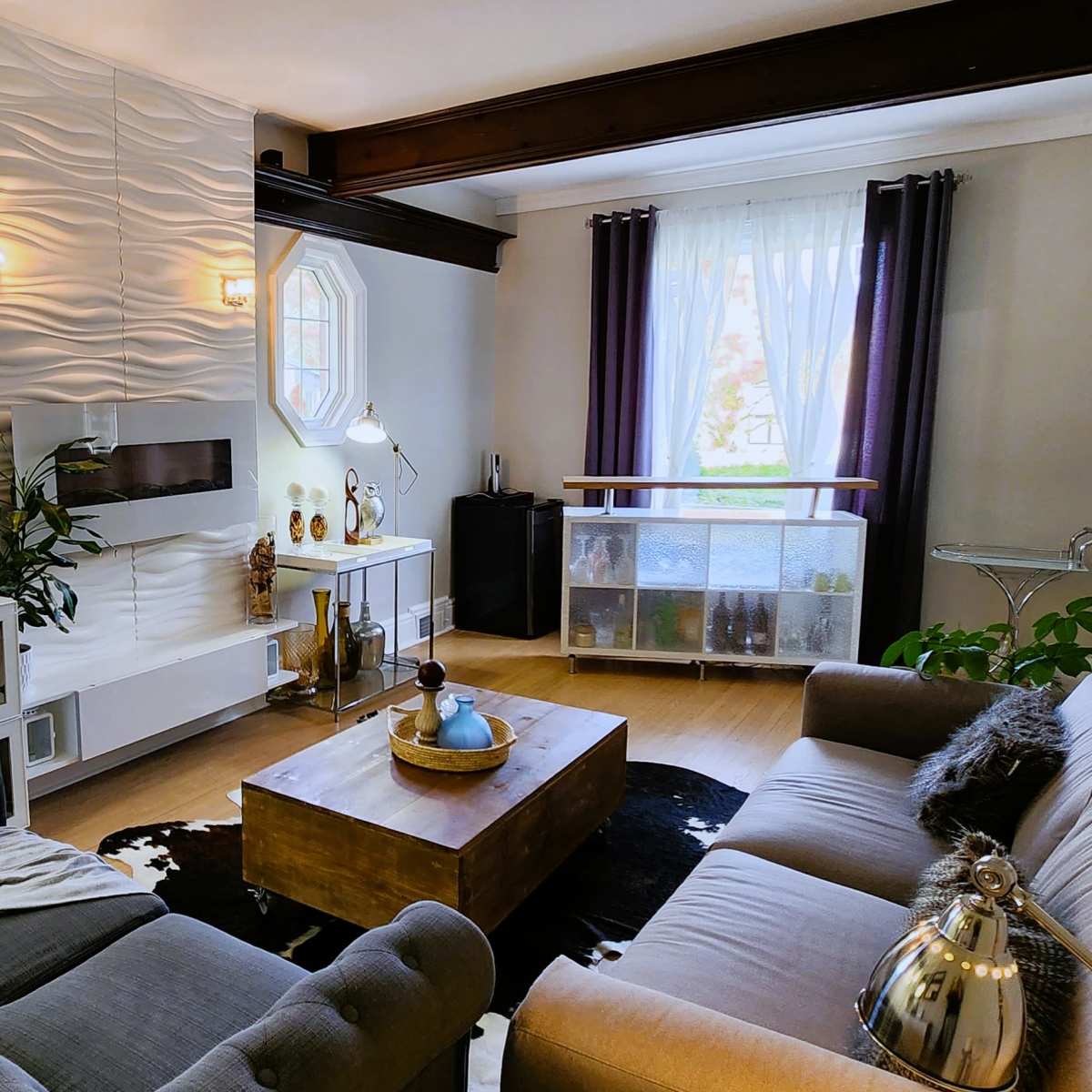 A living room featuring a sectional sofa, a wooden coffee table, a modern entertainment unit, and large windows with light curtains.