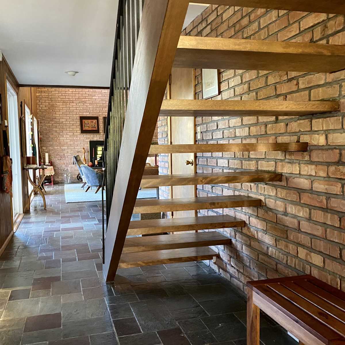 A spacious interior with a wooden staircase, brick walls, and a sitting area visible in the background.