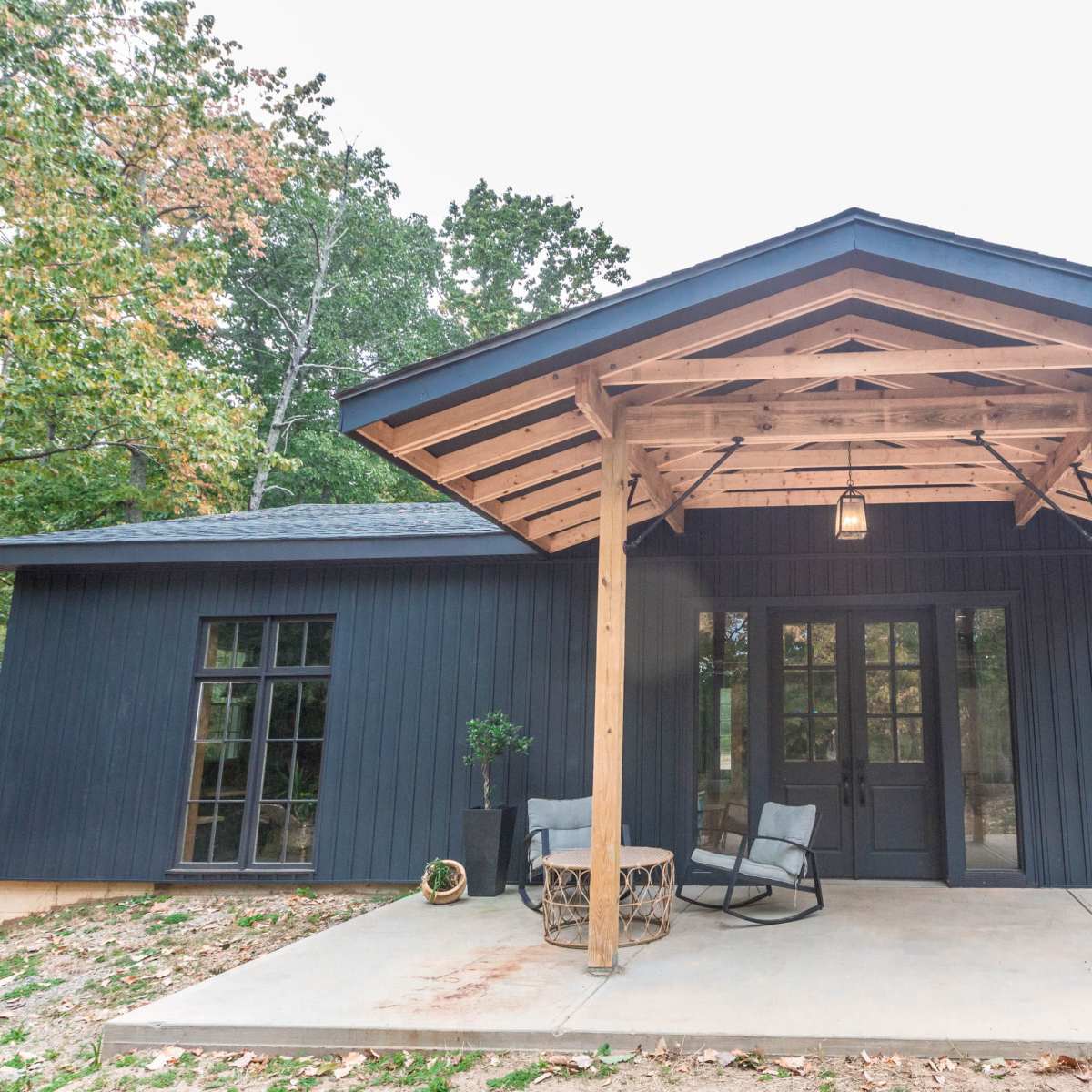 A modern house with a blue exterior and a wood-beamed porch, featuring two chairs and a small round table.