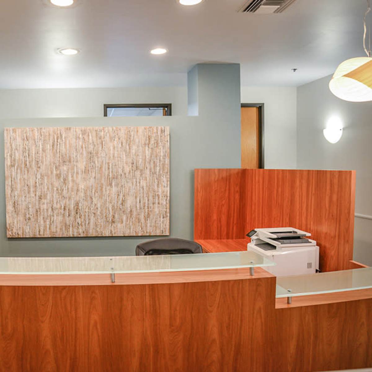 A reception area features a wooden front desk, a printer, and a large abstract wall art piece.