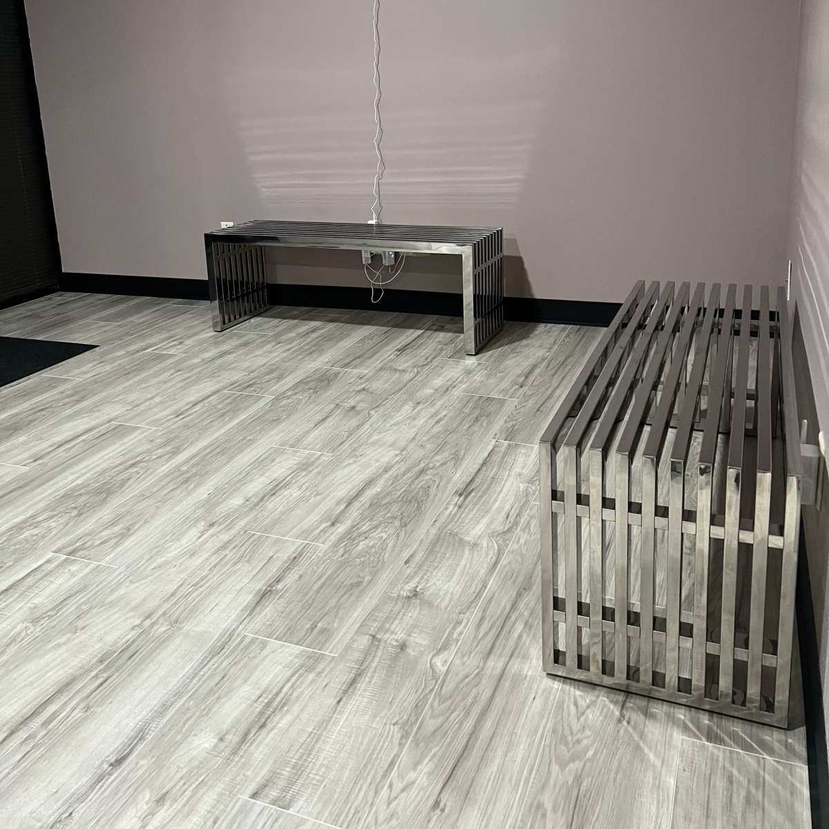 A simple interior space featuring two modern metallic benches on a wooden floor with a plain wall in the background.