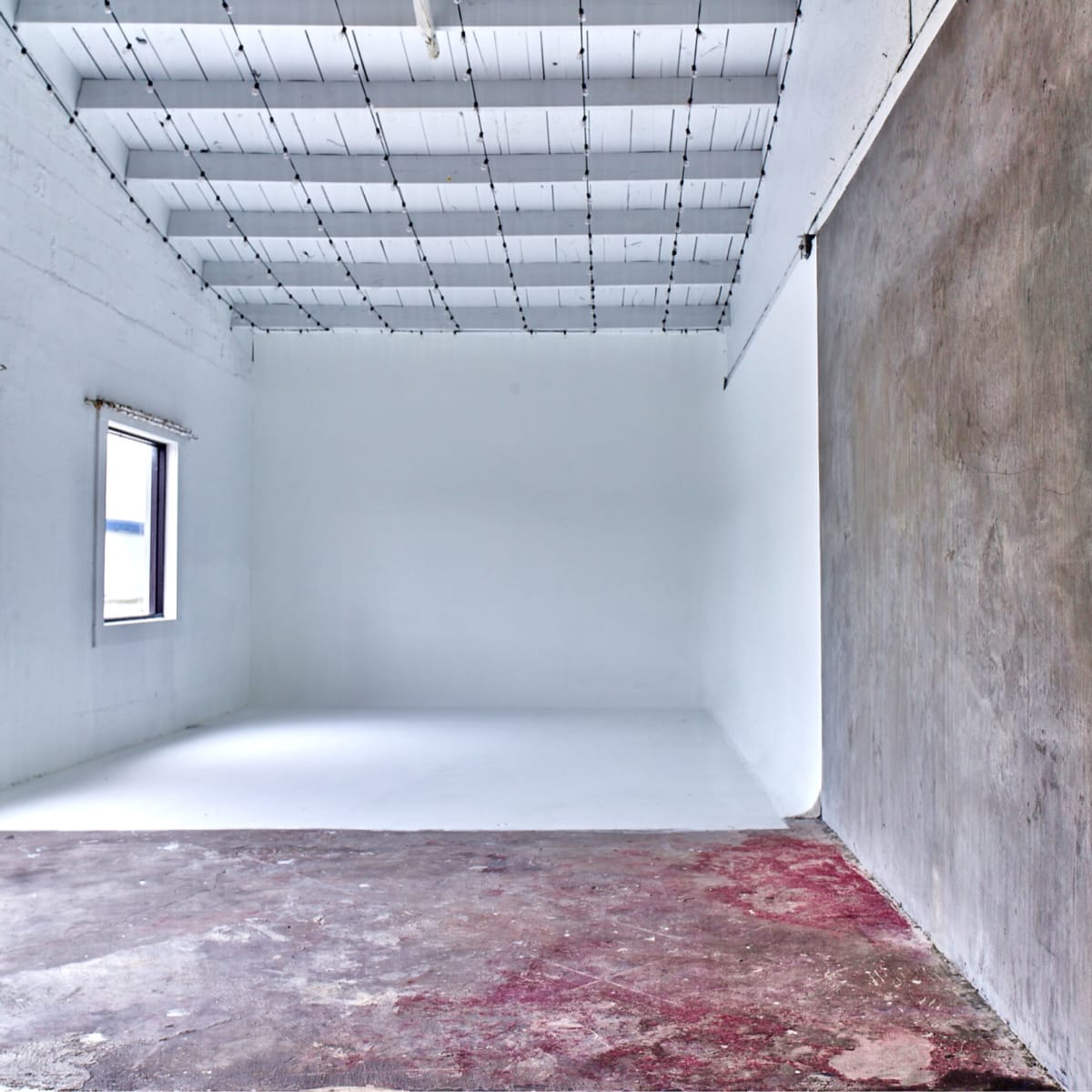 An empty room with white walls, a concrete floor, and two windows on one side.