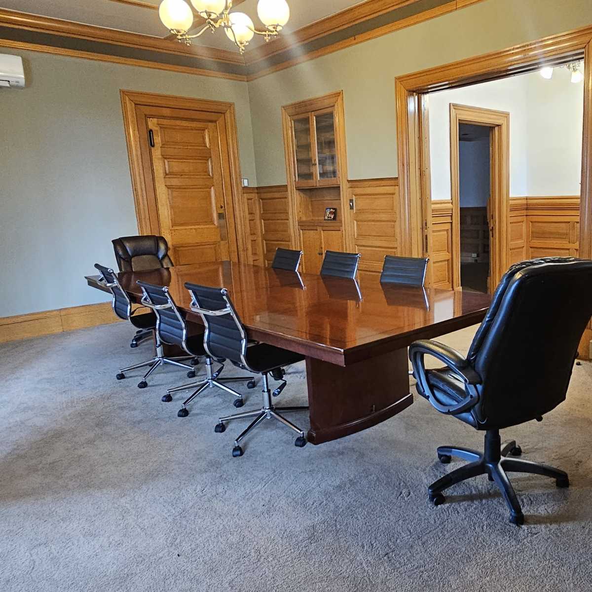 A spacious meeting room with a large wooden table surrounded by black chairs, and wooden paneling on the walls.