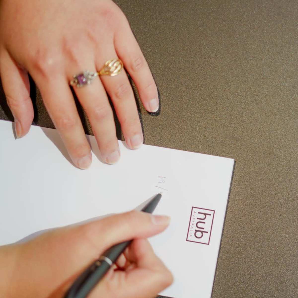 A person's hands are writing on a piece of paper placed on a round table with the word "hub" printed on it.