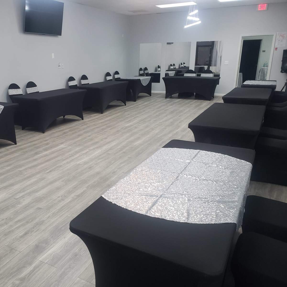 A spacious event room featuring several tables covered with black and silver tablecloths arranged in a neat layout.