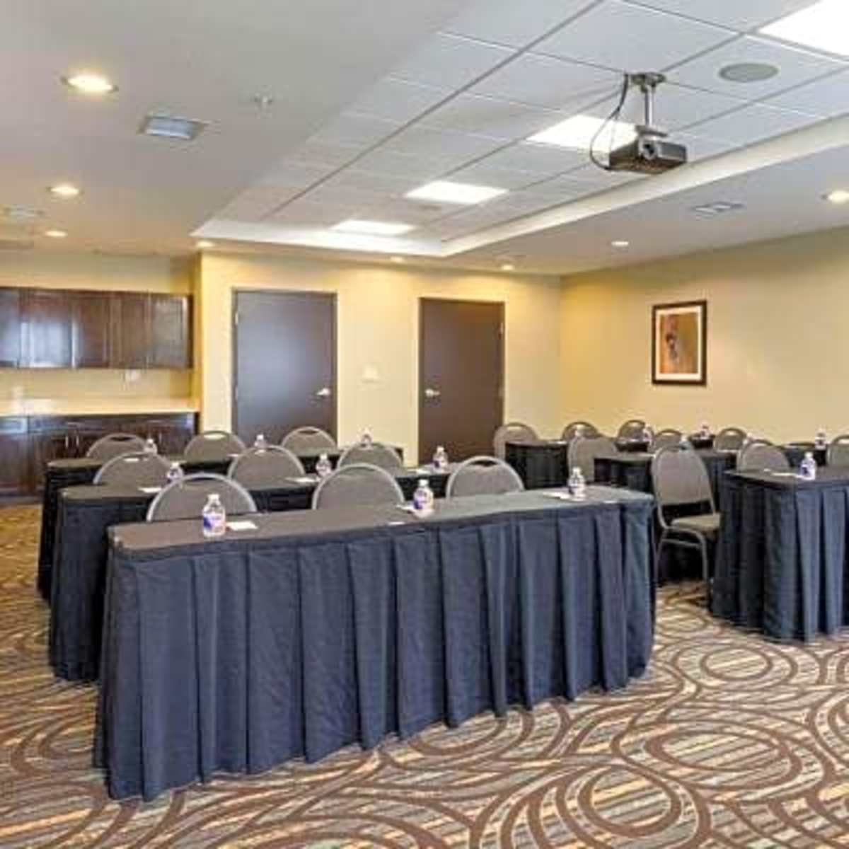 A conference room is set up with rows of tables covered in black cloth, each containing a water bottle, and a projector mounted on the ceiling.