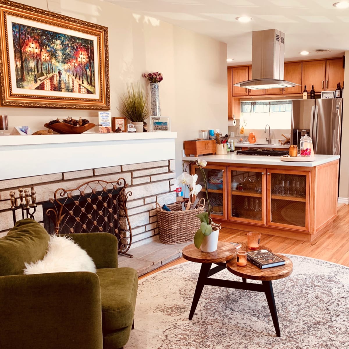 A cozy living room with a green sofa, a round coffee table, and a kitchen area in the background featuring wooden cabinetry and stainless steel appliances.