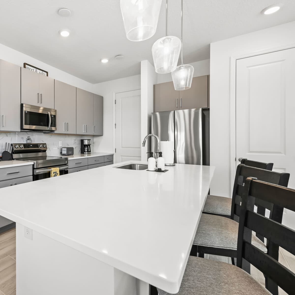 A modern kitchen features gray cabinets, stainless steel appliances, and a white countertop with bar seating.