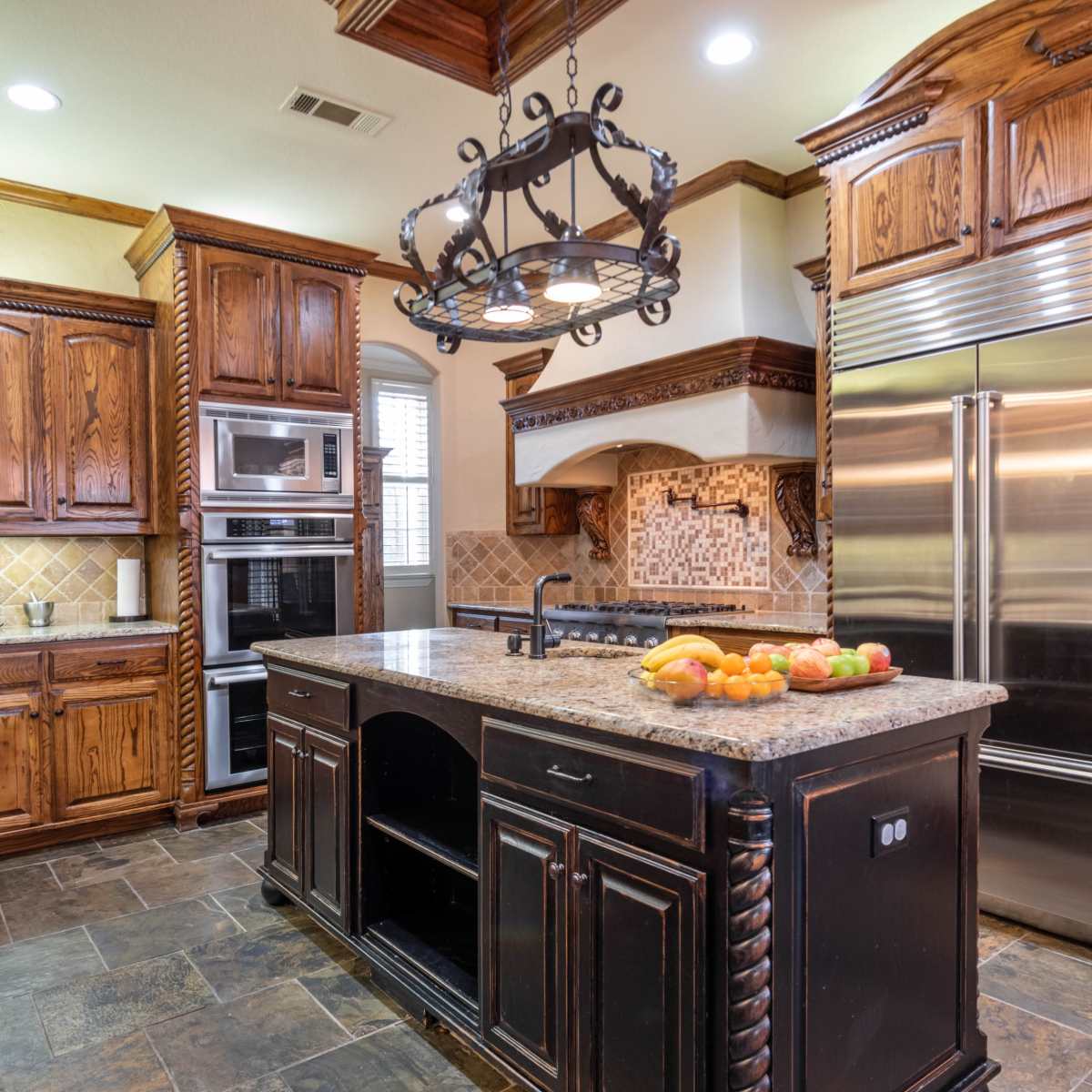 A kitchen with wooden cabinets, stainless steel appliances, and a central island topped with a bowl of fruit.