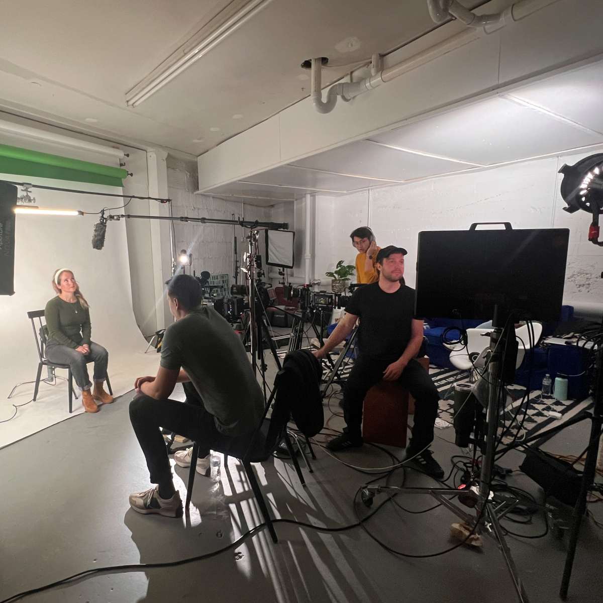 A film crew is recording an interview in a studio equipped with lights, cameras, and sound equipment.
