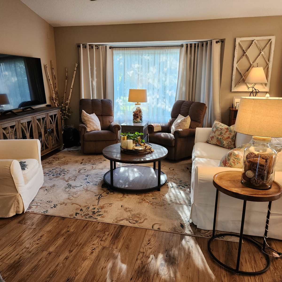 A cozy living room features two recliners, a coffee table with decorative items, and large windows letting in natural light.