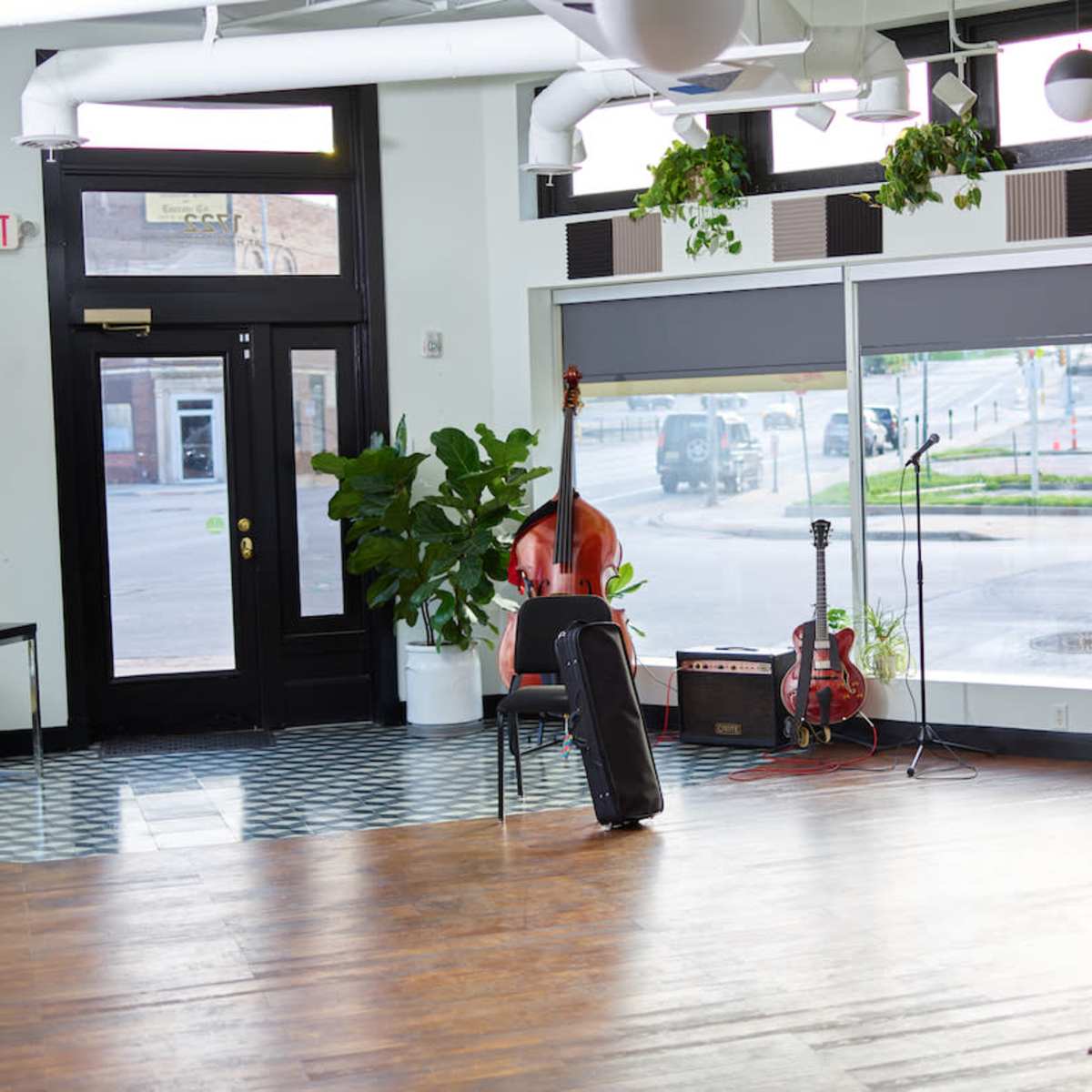 A spacious interior with wooden floors, a microphone stand, and musical instruments near a large window lined with plants.