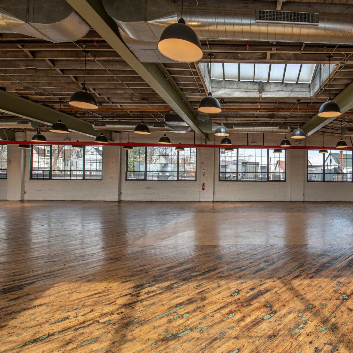 A spacious, empty industrial-style room with large windows and wooden floors.