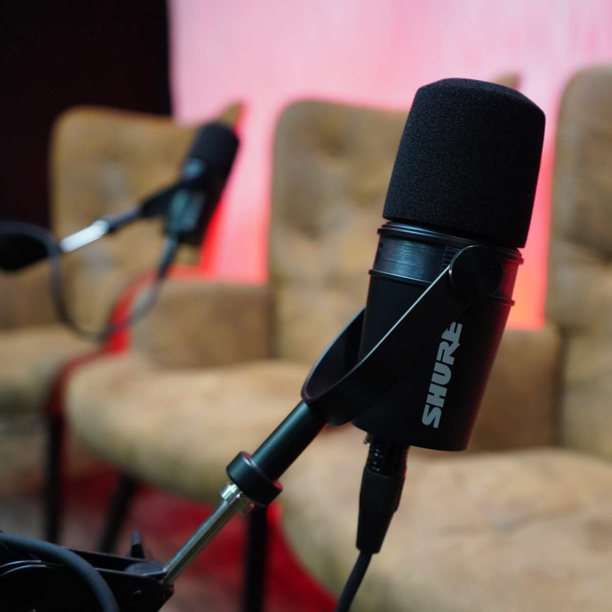 A black Shure microphone is positioned in front of two upholstered chairs against a softly lit background.