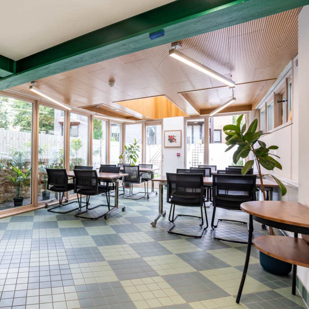 A bright, modern meeting room with green and blue tiled flooring, surrounded by large windows and office furniture.