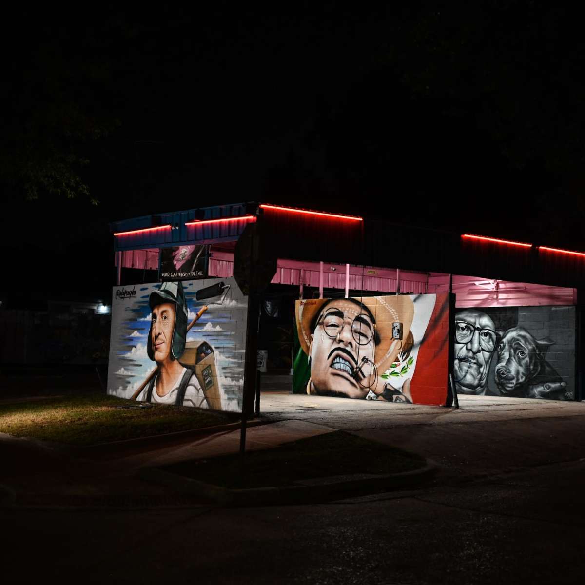 A building at night displays vibrant murals on its exterior walls, highlighted by neon red lights.
