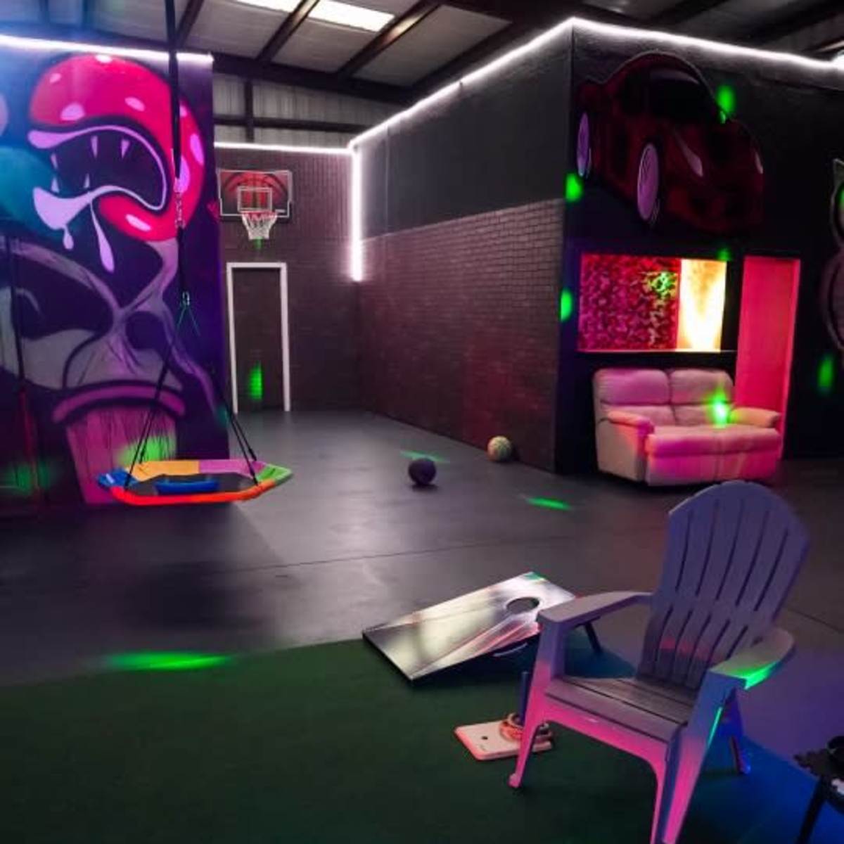 A recreational indoor space featuring a basketball hoop, a swing, colorful lighting effects, and a seating area with a couch.