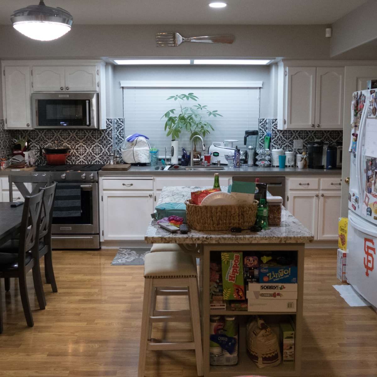 A kitchen features a dining table, modern appliances, and a refrigerator surrounded by various items and a plant on the counter.