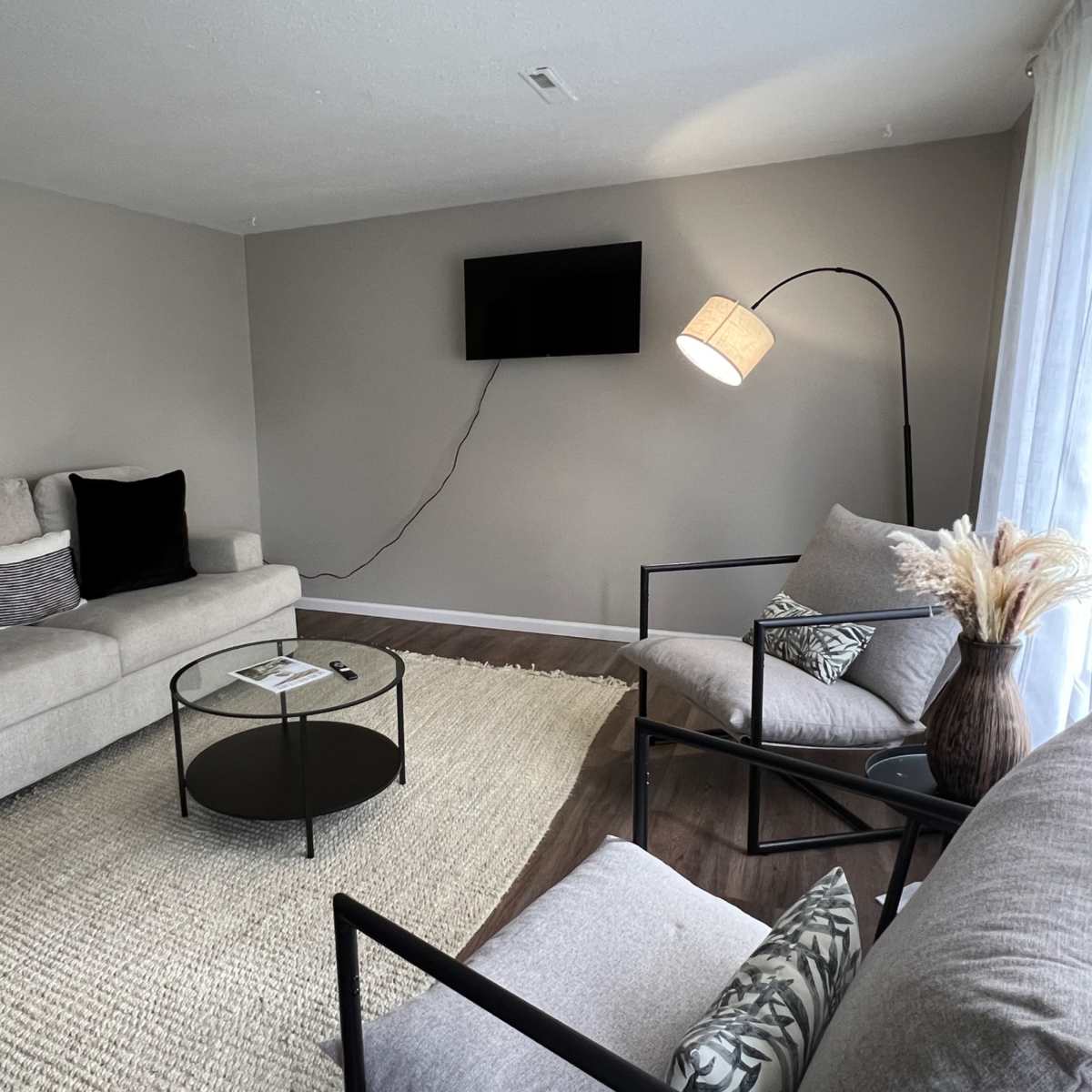 A living room with two sofas, a black coffee table, a floor lamp, and a television mounted on the wall.