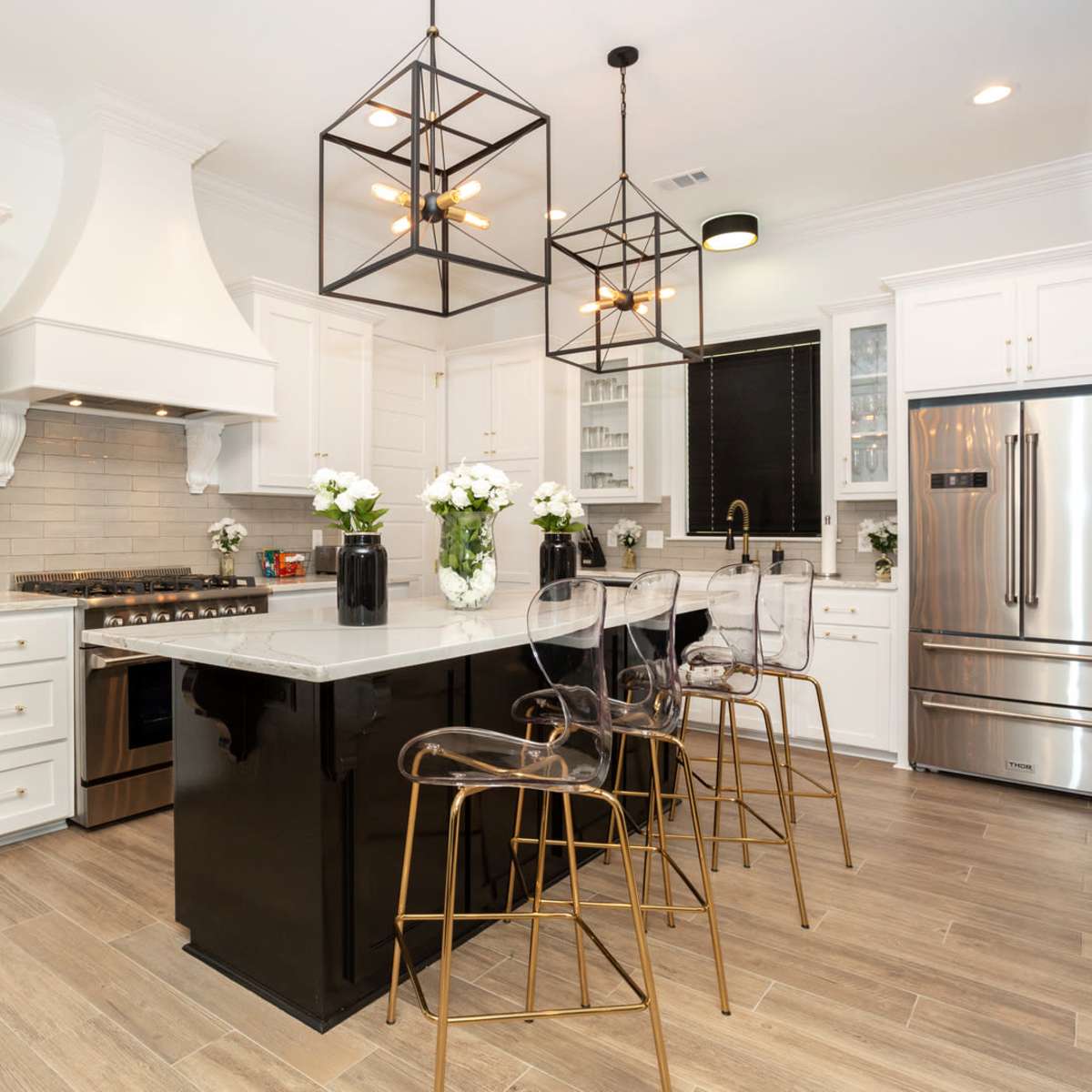 The kitchen features white cabinetry, a large central island with bar seating, stainless steel appliances, and industrial-style light fixtures.