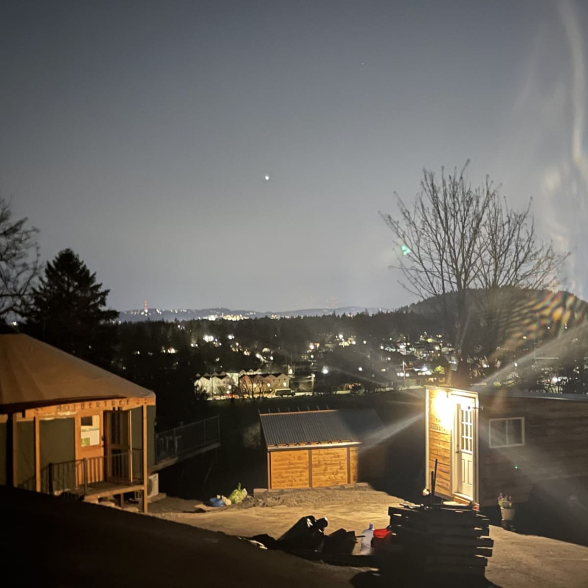 A brightly lit cabin stands on a hillside overlooking a city illuminated by night lights.