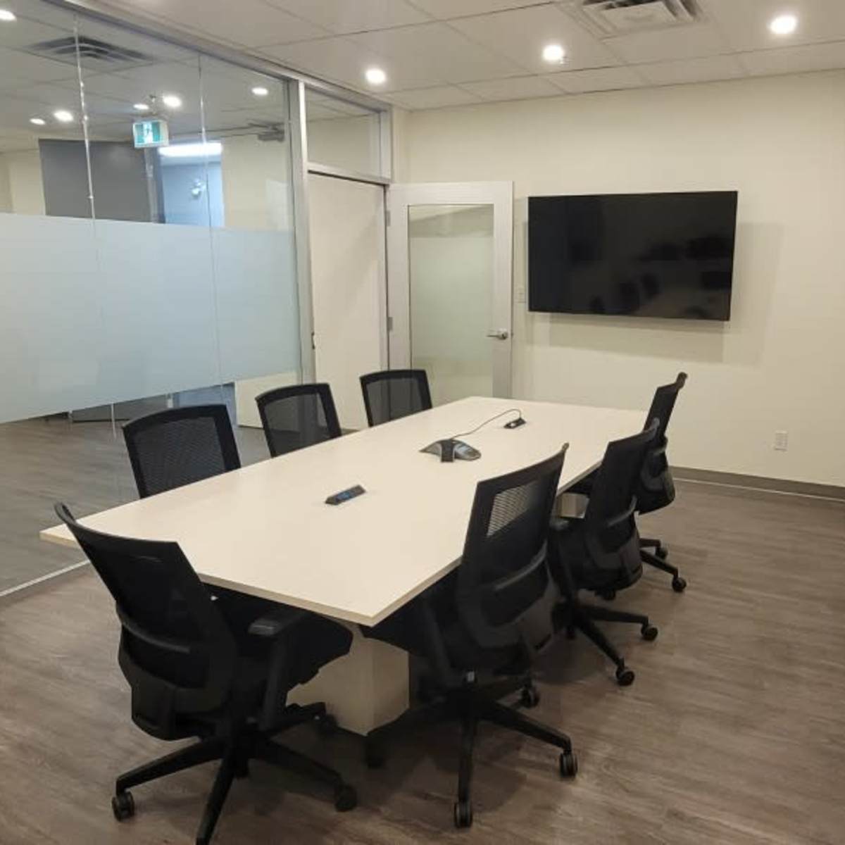 A modern conference room with a long table, several black chairs, and multiple wall-mounted screens.