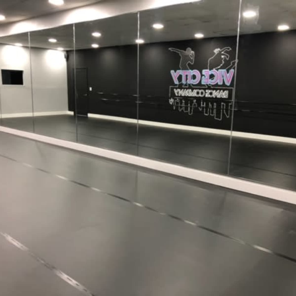 A dance studio with mirrored walls, a black backdrop, and a smooth gray floor.