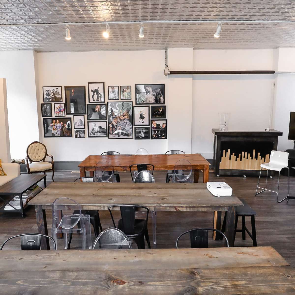 A spacious, well-lit room featuring wooden tables, a sofa, and walls adorned with framed photographs.