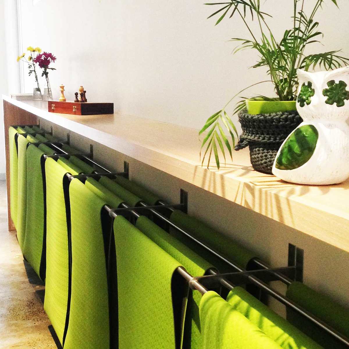 A long wooden shelf holds several green yoga mats and a decorative plant, with a small bouquet of flowers and other items arranged on top.