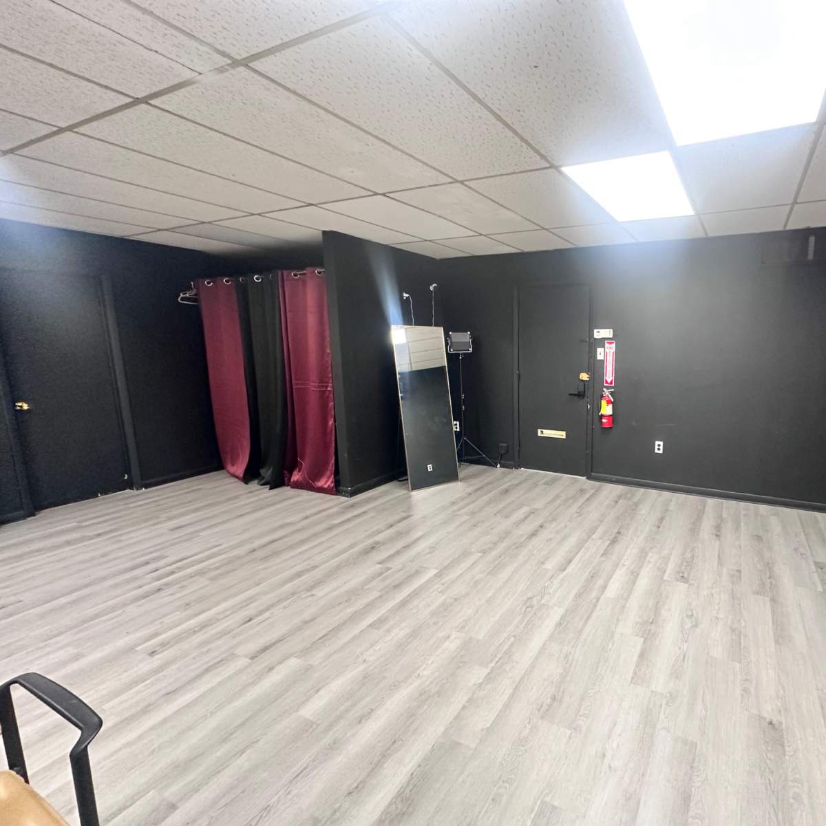 An empty room with black walls and a gray laminate floor, featuring a door, a window, and curtains.