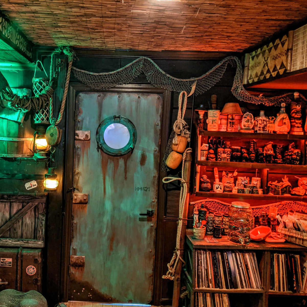 A dimly lit, themed room featuring a porthole door, various nautical decorations, and shelves filled with collectibles.