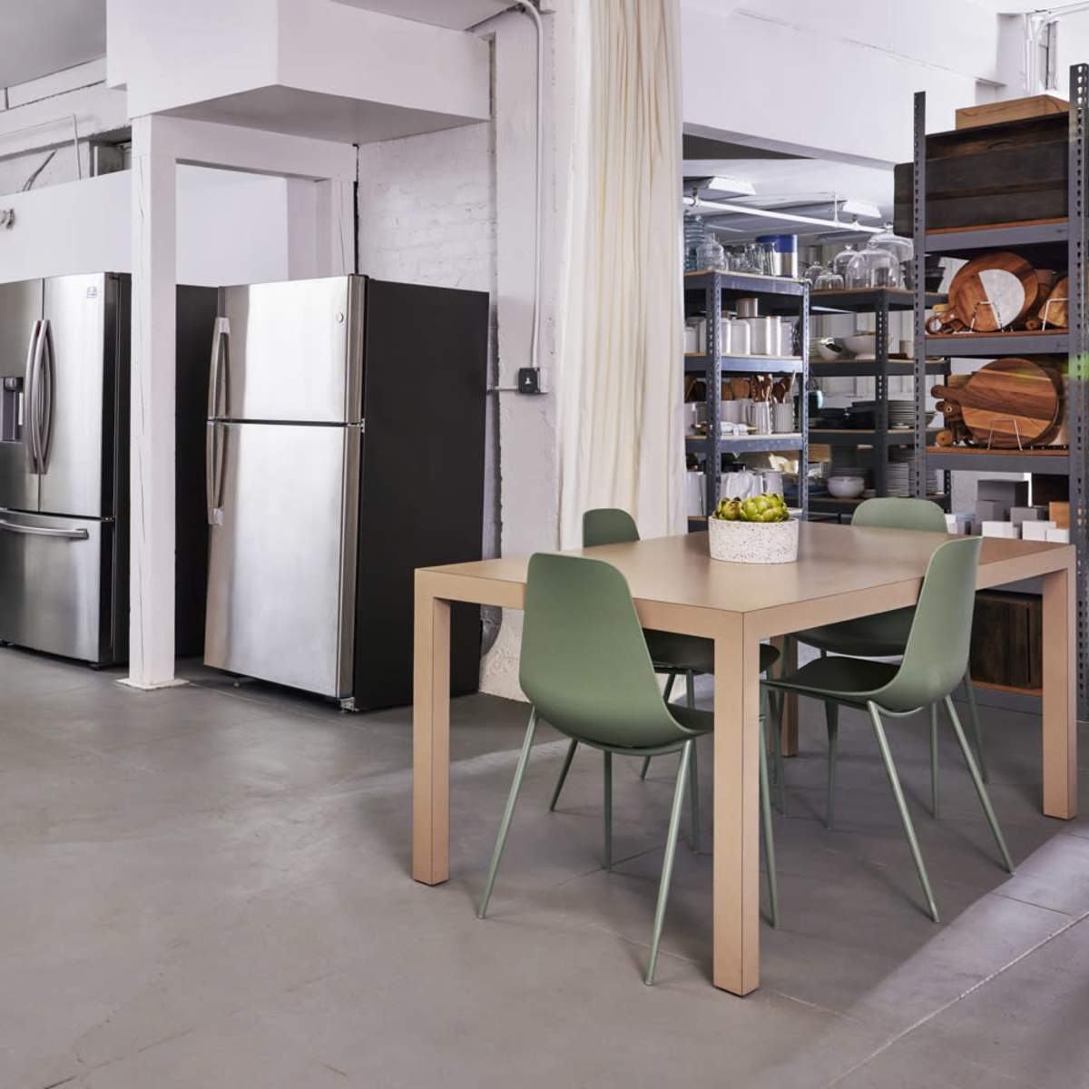 A modern kitchen space featuring stainless steel refrigerators, a dining table with green chairs, and a shelving unit filled with various kitchen items.