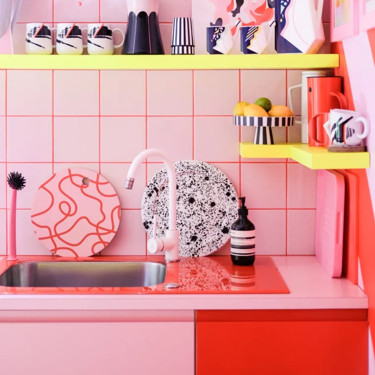 A vibrant pink kitchen features patterned dishware and art displayed on colorful shelves above a sink.