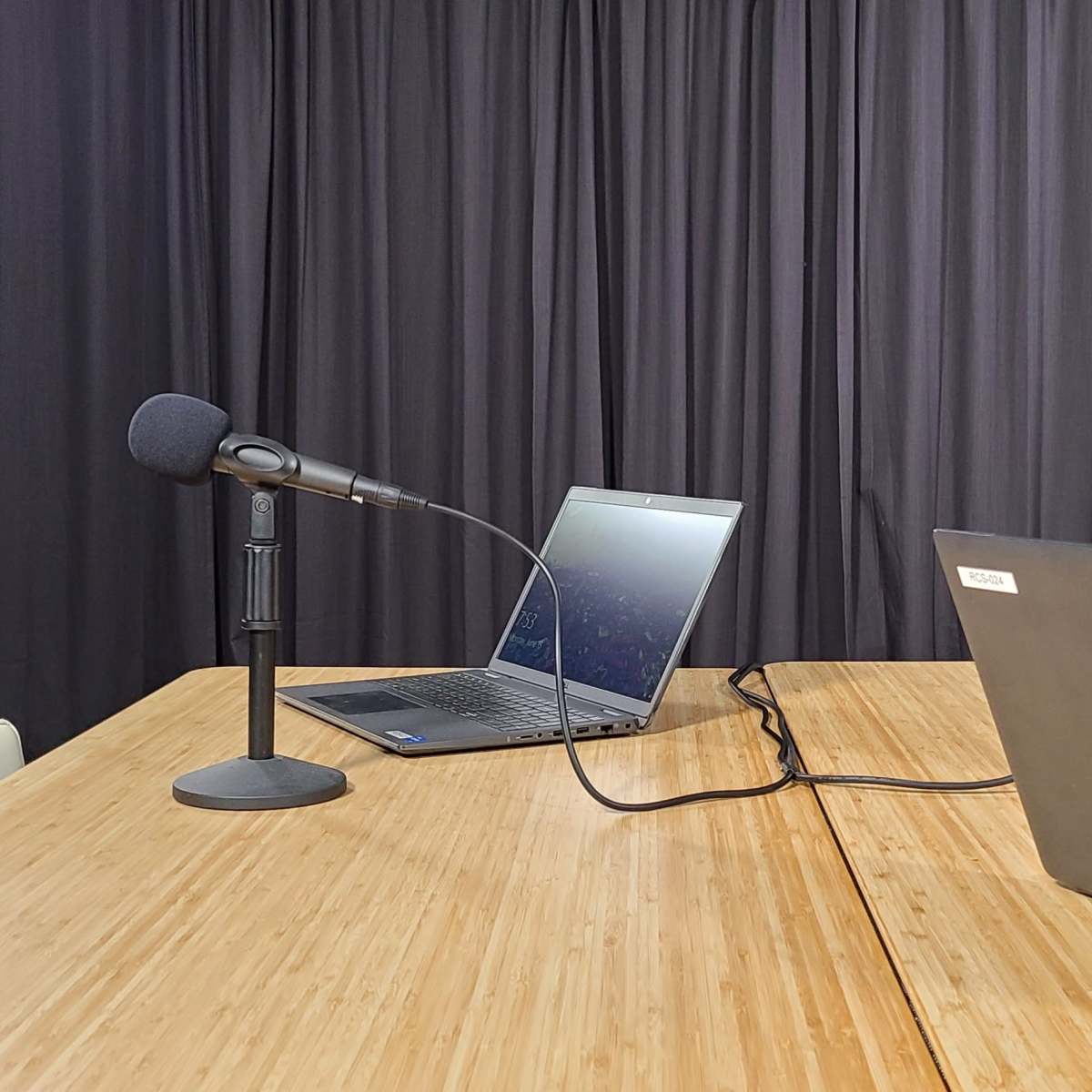 A wooden table with two laptops and microphones set up in front of a black backdrop.