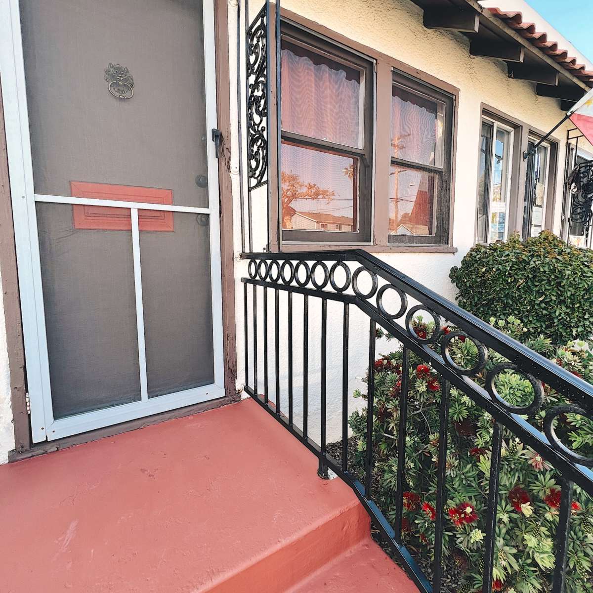 A front entrance with a screened door, a decorative railing, and a red-painted step leading to a small garden area.